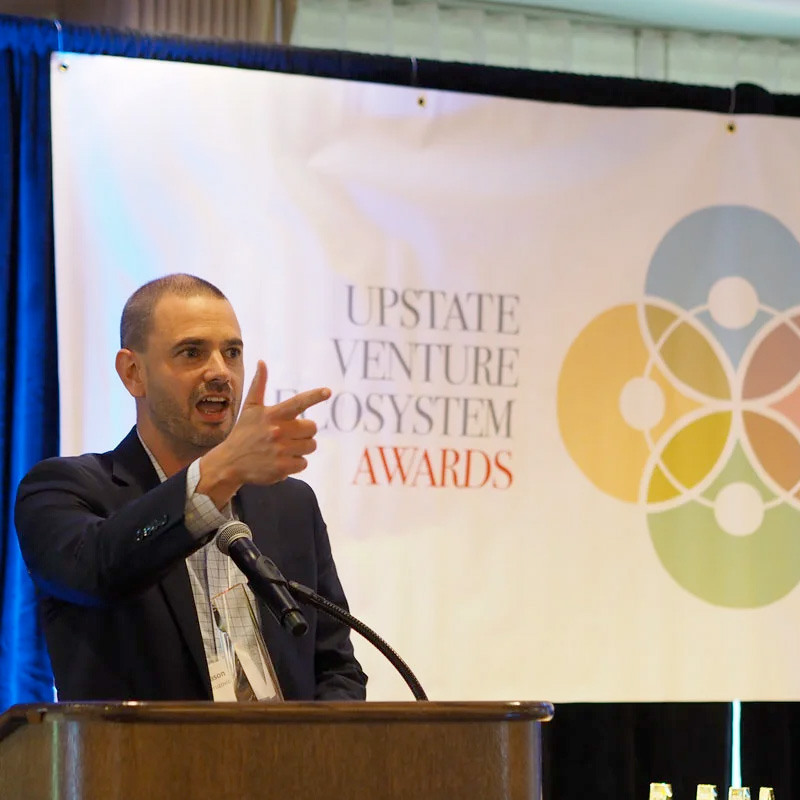 Professor at podium announcing Upstate Venture Ecosystem Awards